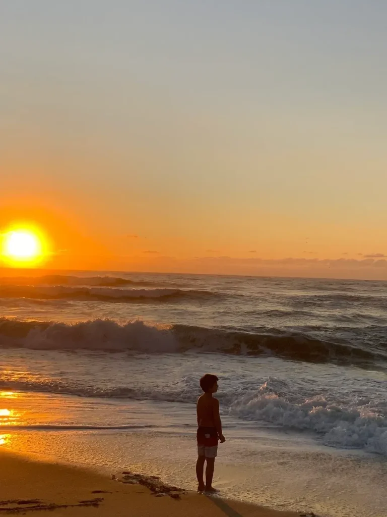 a boy at the sea shore while the sun is setting